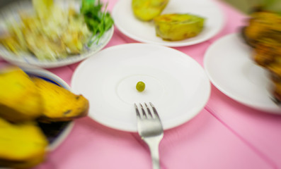 The concept of starvation, bulimia. A pea on a fork surrounded by blurry dishes.