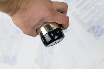 A man's hand holds a mechanical timer against the background of scattered papers. The concept of...