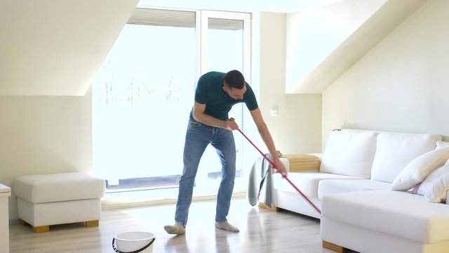 people, housework and housekeeping concept - happy man with mop cleaning floor and dancing at home