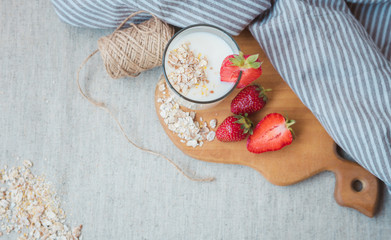 a glass with yogurt oatmeal flakes, pieces of strawberries and a bunch of acacia on a wooden cutting board. a glass of milk with strawberries.