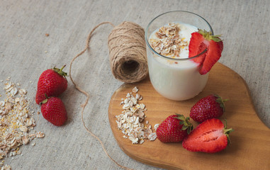 a glass with yogurt oatmeal flakes, pieces of strawberries and a bunch of acacia on a wooden cutting board. a glass of milk with strawberries.