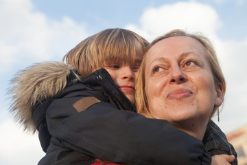 Happy and proud mother carries her little son in the back