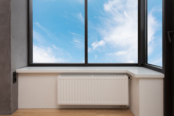 Heating white radiator with adjuster of warming in living room under a large window.