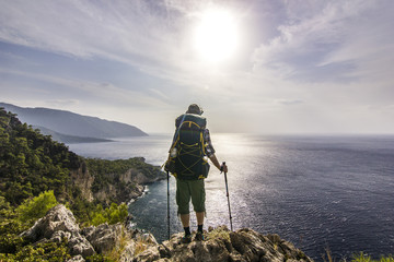 tourist with backpack standing on a cliff in mountains near mediterranean sea