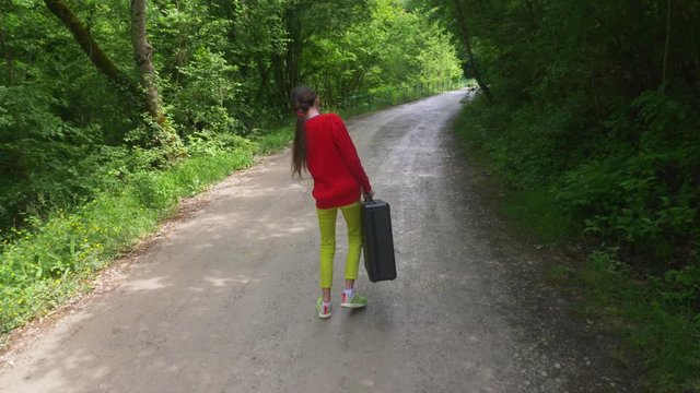 girl, walks through the woods with a heavy black suitcase. 4k, slow-motion shooting, steadicam shot.