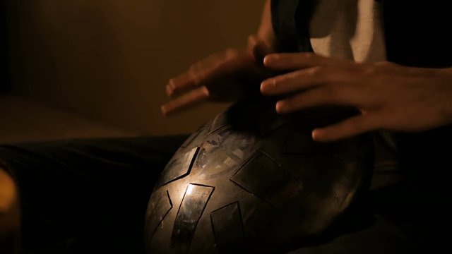 Man playing tank drum or hang at home. Warm romantic illumination, low key. Relaxation, meditative and traditional music concept. Close up shot