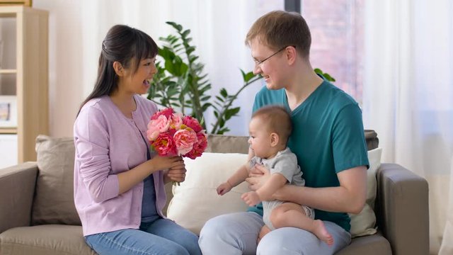 family, parenthood and mothers day concept - happy mother receiving flower bunch from father and baby boy at home