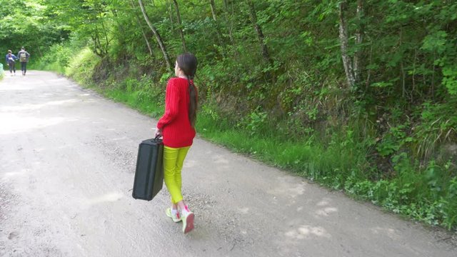 girl, walks through the woods with a heavy black suitcase. 4k, slow-motion shooting, steadicam shot.