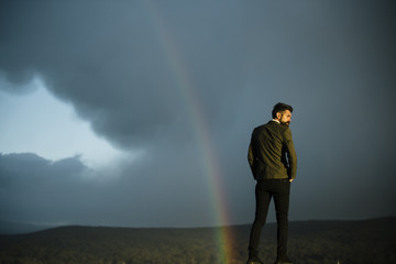 Man and rainbow on grey sky. Man with beard and mustache on vacation, copy space