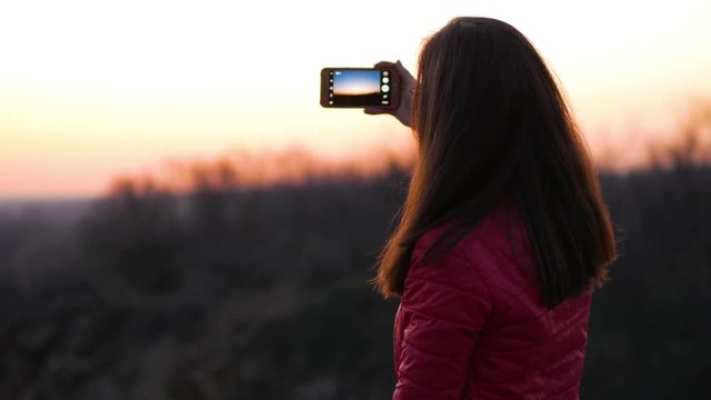 Young woman taking pictures with her smartphone at sunset.