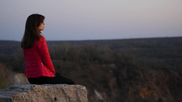 Young girl in a red jacket sitting on the rocks and looking into the distance
