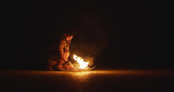Wanderer with a beard sits by the fire and throws up wood at night