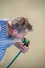  man drinks water from a hose on a hot day