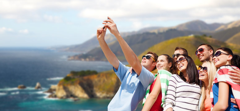 travel and tourism concept - group of happy friends taking selfie by cell phone over big sur coast of california background