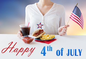 independence day, celebration, patriotism and holidays concept - close up of woman hands with hot dog and french fries holding american flag and cola drink at 4th july party over sky background