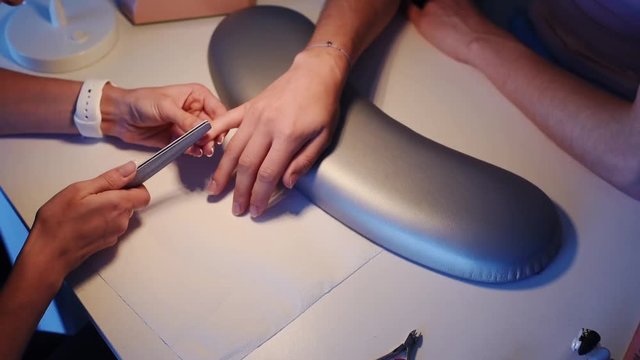 Closeup of female hands in a nail salon receiving a manicure by a beautician with nail file. Beautician file nails to a customer.