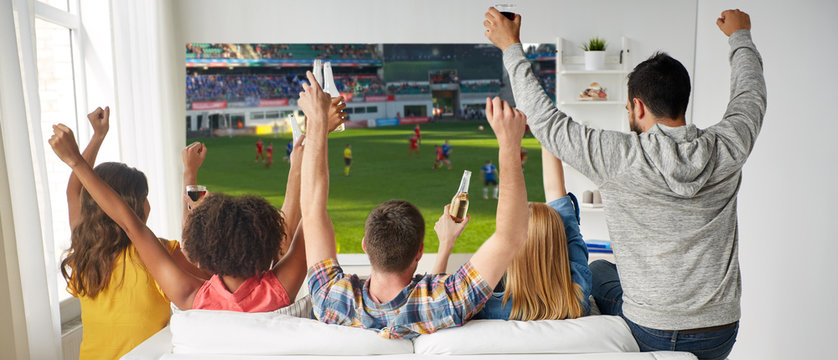 leisure, sport and people concept - happy friends with bottles of non-alcoholic beer watching soccer or football on projector screen at home