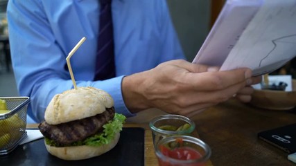 Young businessman eating snack and working with documents at cafe
 - Powered by Adobe