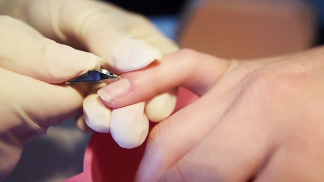 Close-up of nail master hands in disposable gloves cutting cuticles by using manicure cutters on client’s fingers. Slow motion.