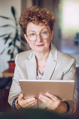 portrait of an attractive middle aged woman holding a tablet. fashionable mature lady using a tablet in her home office, working from home as a creative. businesswoman reading email at home.