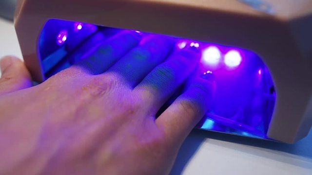 Close-up of woman putting her hand in led lamp to dry the gel nail polish. Hand in drying tool.