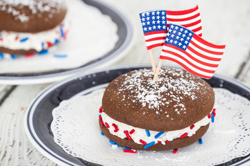 Whoopie pie or moon pie, chocolate cake dessert filled with creamy frosting. Decorated with American flags and red, white, and blue sprinkles in celebration of the 4th of July.