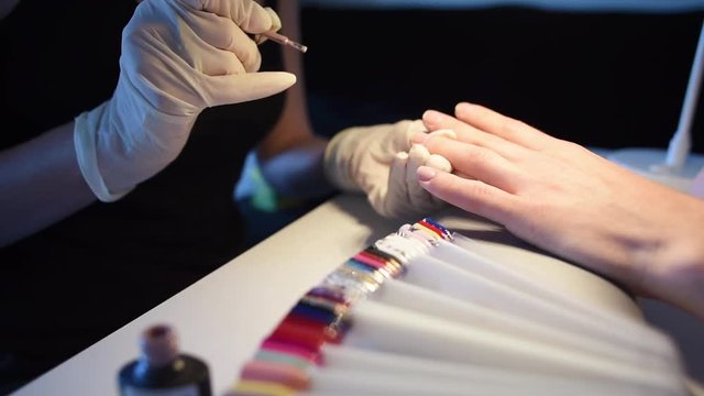Nail master in disposable gloves deciding what nail to paint with a pastel gel nail polish. Slow motion.