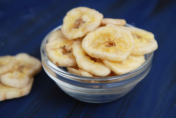 Healthy snack made from Banana Chips. Sliced Banana pieces in Glass bowl on Dark blue Background.