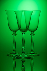 Glasses on a high leg on the mirror surface of the table, on a green background.