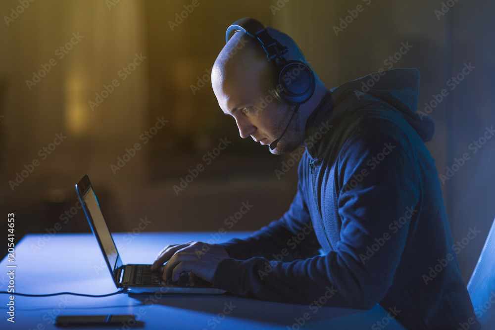 Poster cybercrime, hacking and technology concept - male hacker with headset using laptop computer for cybe