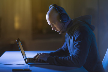 cybercrime, hacking and technology concept - male hacker with headset using laptop computer for...