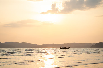 Beautiful summer sunset over sea with sunbeam through clouds above mountain and fishing boat.