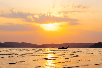 Beautiful summer sunset over sea with sunbeam through clouds above mountain and fishing boat.