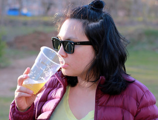 girl in dark glasses drinking beer from a plastic glass