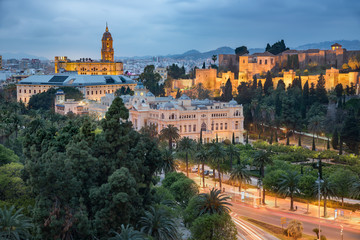Fototapeta premium Malaga old town skyline with the city hall, cathedral and the Alcazaba citadel taken at the blue hour in a cloudy day, Andalucia, Spain