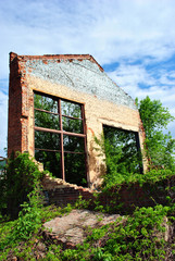 Old crumbling brick wall with window without glass, green trees and blue cloudy spring sky