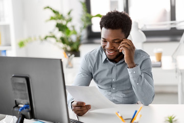 business, people, communication and technology concept - smiling african american businessman with papers and computer calling on smartphone at office