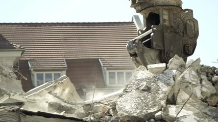 Close up tracking shot of an industrial hydraulic demolition claw demolishing an old concrete and re-bar structure to make way for new construction.