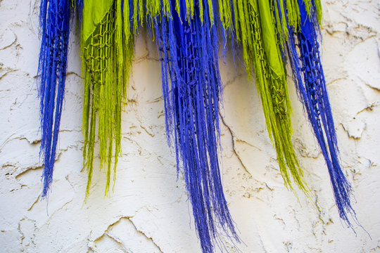 Purple and lime green fringed scarves blow against a rough stucco wall - boho background