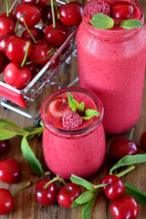 Red smoothie made of cherries in glass jars. Berries are around on a wooden table and in a trolley