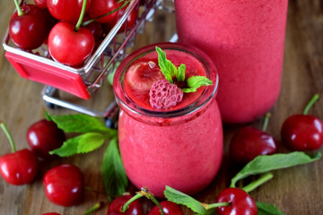Red smoothie made of cherries in glass jars. Berries are around on a wooden table and in a trolley