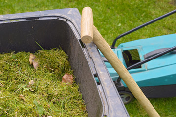 Lawn mower and spade on a bio container with freshly cut grass to recycle