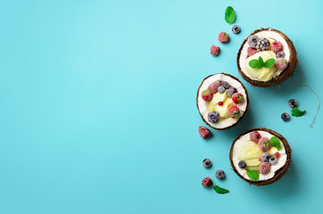 Fototapeta na wymiar Coconut ice cream with fresh berries in coconuts halves on blue background with copy space. Top View. Pop art design, creative summer concept. Food in minimal flat lay style.