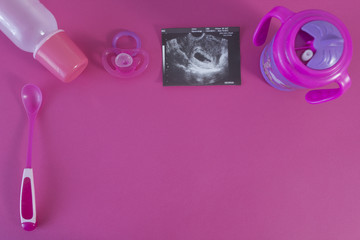 Baby spoon, drinker, nipple and uzi of pregnancy on a pink background