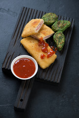 Black wooden serving board with chicken cordon bleu, black stone background, studio shot