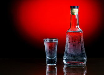 Bottle with glass of vodka on red background