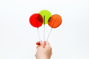 Lollipops on a stick - red, green and orange in hand on a white background.