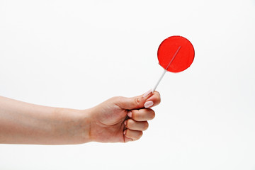 Red round lollipop on a stick in a hand on a white background.