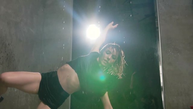 Wet girl dancer or ballerina in black body suit and points performs contemporary dance on the floor in the rain and splashes of water. The ballerina who perform dance under the water on on the floor