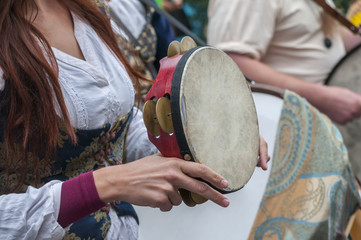 Side view of girl in medieval costume plays tambourine in the street